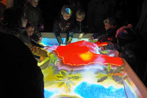 Grote groep kinderen die om de interactieve zandtafel van Dinoland staat te spelen.